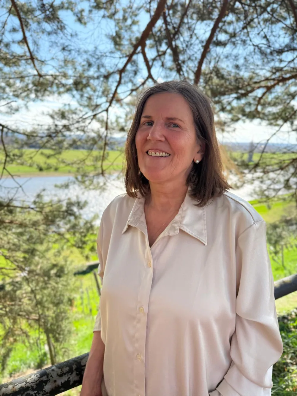 Irene Herrera Krebber lächelt, im Hintergrund Bäume und ein Fluss