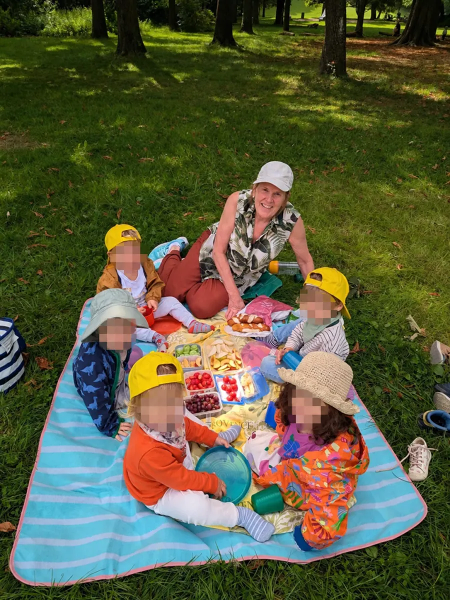 Irene macht mit den Kindern ein Picknick auf einer Decke im Stadtpark