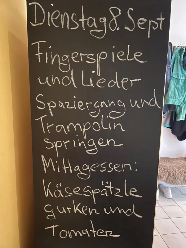 Kreidetafel mit dem Tagesplan: Fingerspiele und Lieder, Spaziergang und Trampolinspringen, mittags Käsespätzle mit Gurken und Tomaten